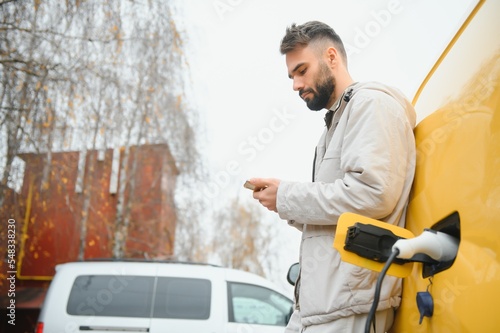 Casual man near electric car waiting for the finish of the battery charging process