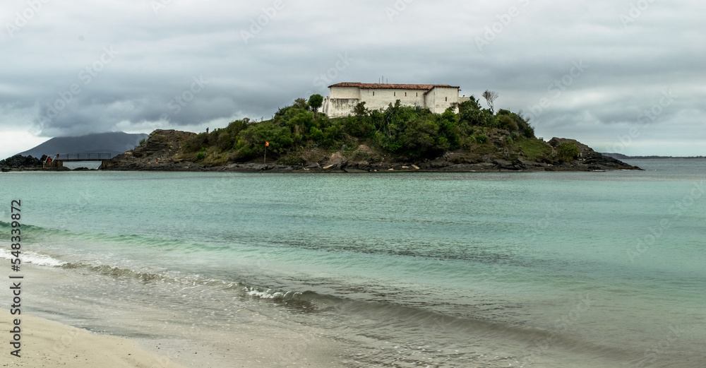 Obraz premium Praia do Forte, com o forte no topo de monte, mar, grandes rochas e céu com nuvens.