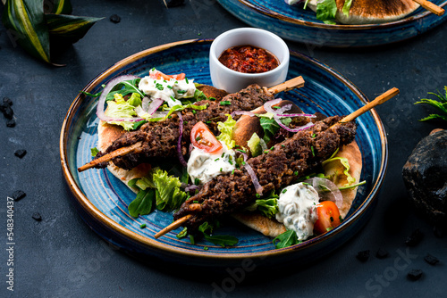 Fresh kebab, barbecued beef on a stick with tomatoes, lettuce, onion, arugula, sour cream, tortilla and red sauce.