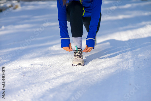 Close up of caucasian woman crouching and adjusting sneaker before running at snowy winter day
