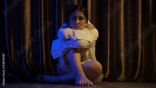 young girl in white shirt sitting on the floor in the dark room blue and yellow light, depression, pain. Domestic violence, family problems, Stress, violence, The concept of depression and suicide. photo