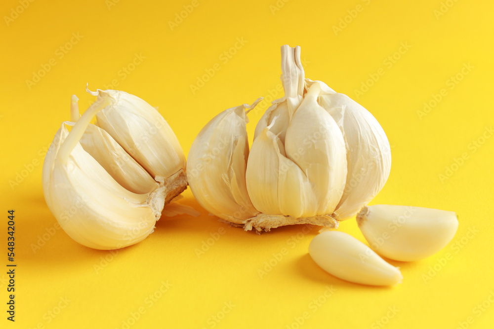 Fresh white unpeeled head bulb of garlic and garlic cloves on yellow