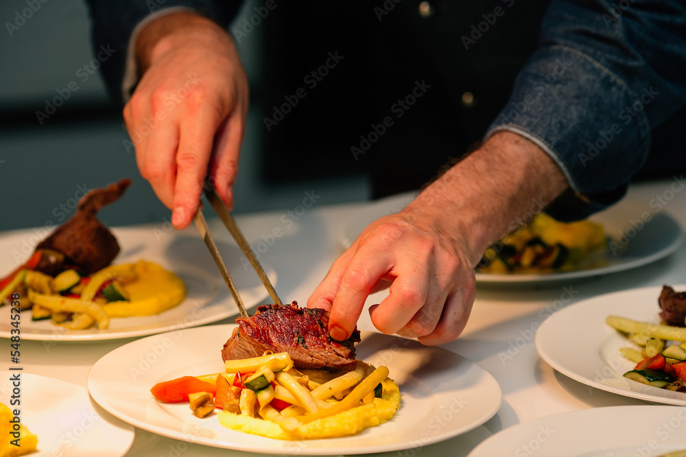 Chef lays out the meat steak on a plate near the grilled vegetables, serves the dish on ordering it at a banquet in a restaurant