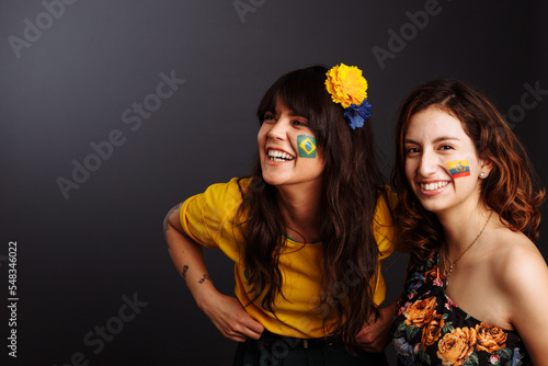 Brazilian and Ecuadorian ladies with body art on their faces looking forward surprized. Colorful painting. Selective focus