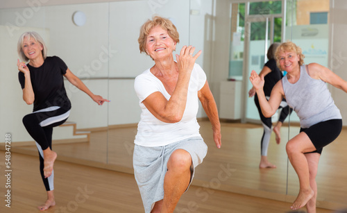 Group of three mature women performing modern dance in exercise room.