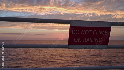 Pink sunrise in ocean. Safety sign foreground DO NOT CLIMB ON RAILING photo