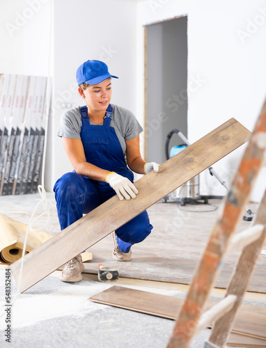 Professional female builder laying laminate flooring in a room being renovated