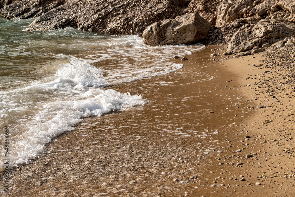 Waves splashing sand beach on Brac island, Croatia creating beautiful, white foam.