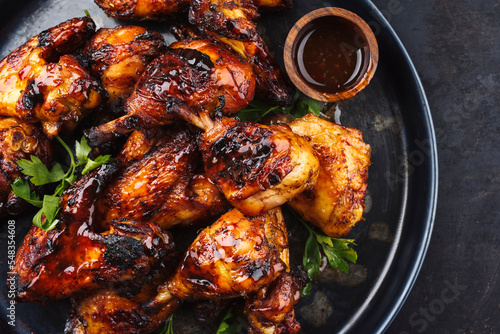 Traditional barbecue chicken wings and drumsticks with hot chili mango sauce and coriander served as top view on a rustic board with copy space right