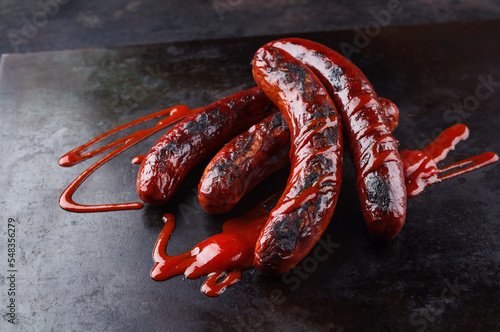 Traditionelle deutsche Bratwurst vom Grill serviert als Draufsicht auf einem rustikalen Holz Board und scharfer Chili Sauce  photo