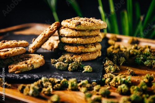 Marijuana cookies, drugs in food, thc and cbd brownies. Drugs and marijuana buds on a plank against the background of growths.