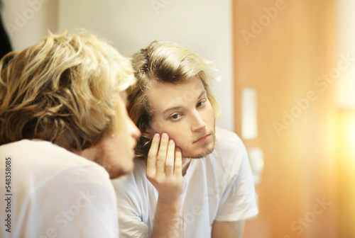 young man looking in the mirror combing his hair looking at problems on face.