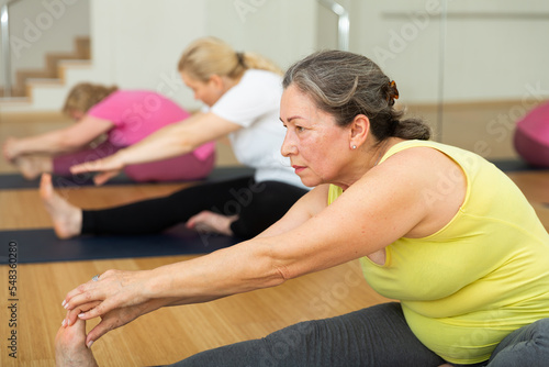 Senior woman maintaining mental and physical health attending group yoga class at studio, practicing stretching poses