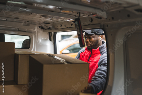 Focused African-American blue-collar-worker - deliveryman - taking out precious cardboard parcels for his clients. Online shopping delivery concept. Van POV. High quality photo