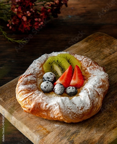 Vertical closeup shot of a gourmet round croissant pastry with powdered sugar and fruits