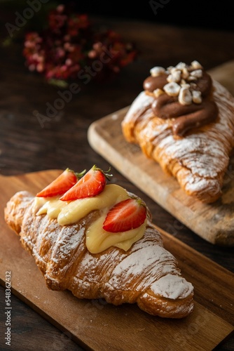 Vertical shot of a gourmet croissant with cream, strawberries and powdered sugar on a board