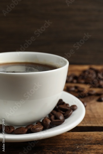 Cup of aromatic coffee and beans on wooden table  closeup. Space for text