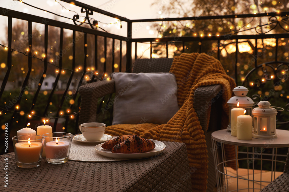 Beautiful view of garden furniture with pillow, soft blanket and burning candles at balcony - obrazy, fototapety, plakaty 