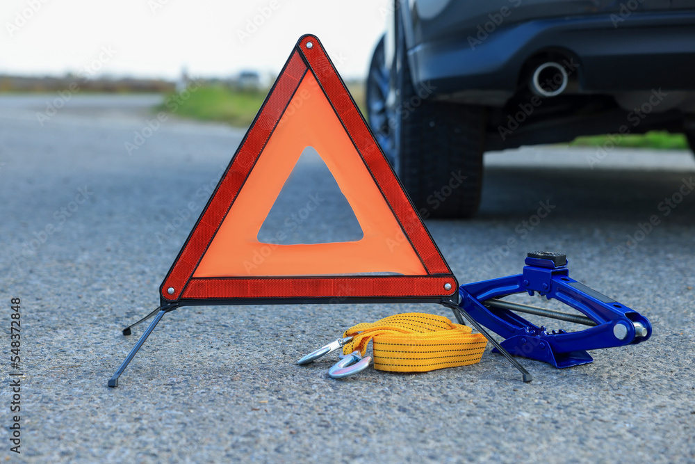 Emergency warning triangle, towing strap and scissor jack near car outdoors. Safety equipment - obrazy, fototapety, plakaty 