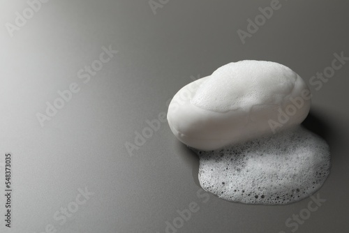Soap with fluffy foam on grey background, space for text