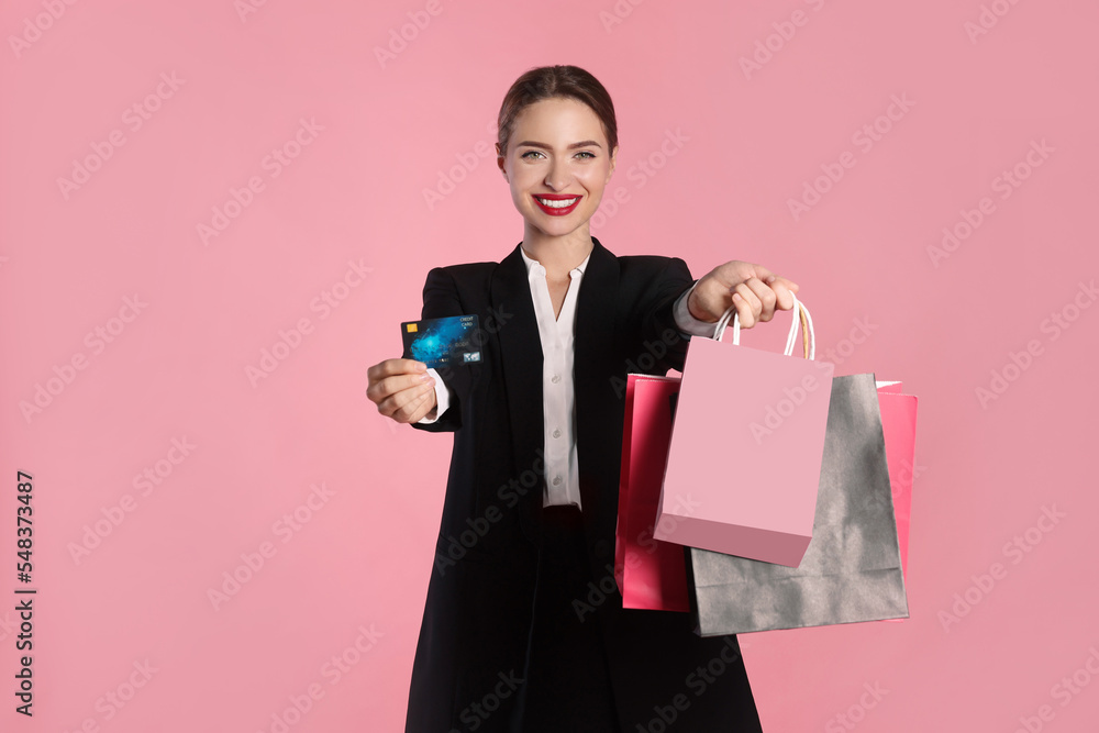 Happy young woman holding shopping bags and credit card against light pink background, focus on hands. Big sale Happy young woman holding shopping bags and credit card against light pink background, focus on hands. Big sale
