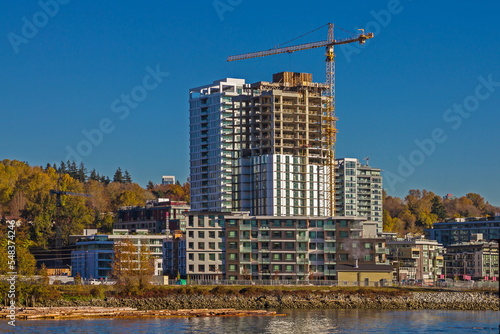 Construction of a new residential district at the riverbank in Vancouver City. The river bank and the slope covered with forest on the background of a cloudy sky