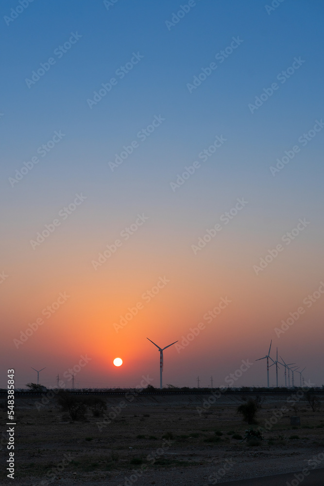 Dawn light in desert sky with Electrical power generating wind mills producing alterative eco friendly green energy for consumption by local people. Sun rise at Thar desert, Rajasthan, India.