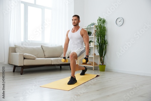 Man sports home training on the floor on a mat with dumbbells, exercises for muscle growth, pumped up man fitness trainer exercises at home, the concept of health and beauty of the body