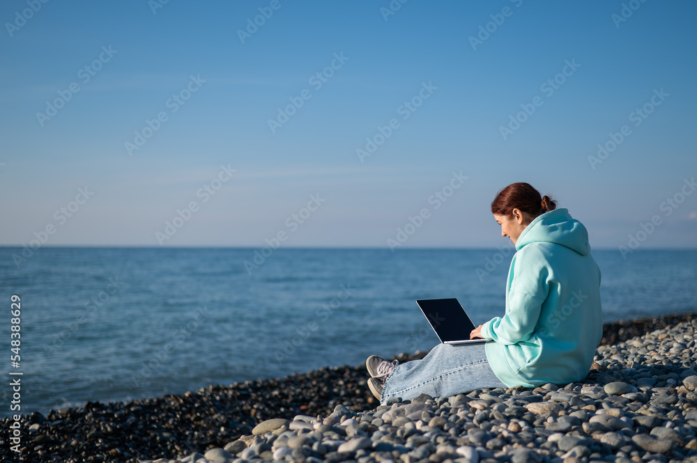 Caucasian woman working freelance on laptop on the beach. 
