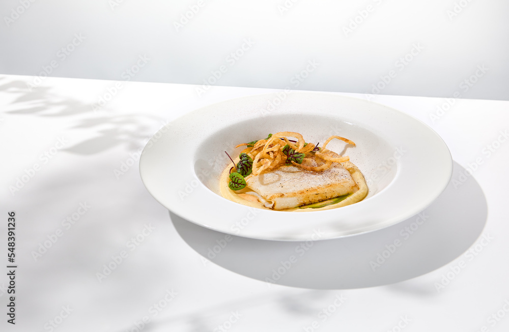 Roasted squid on mashed potatoes and crispy onion. Grilled squid with celery cream on white plate with shadows of leaves. Summer seafood menu. Roasted calamari in fine dining.