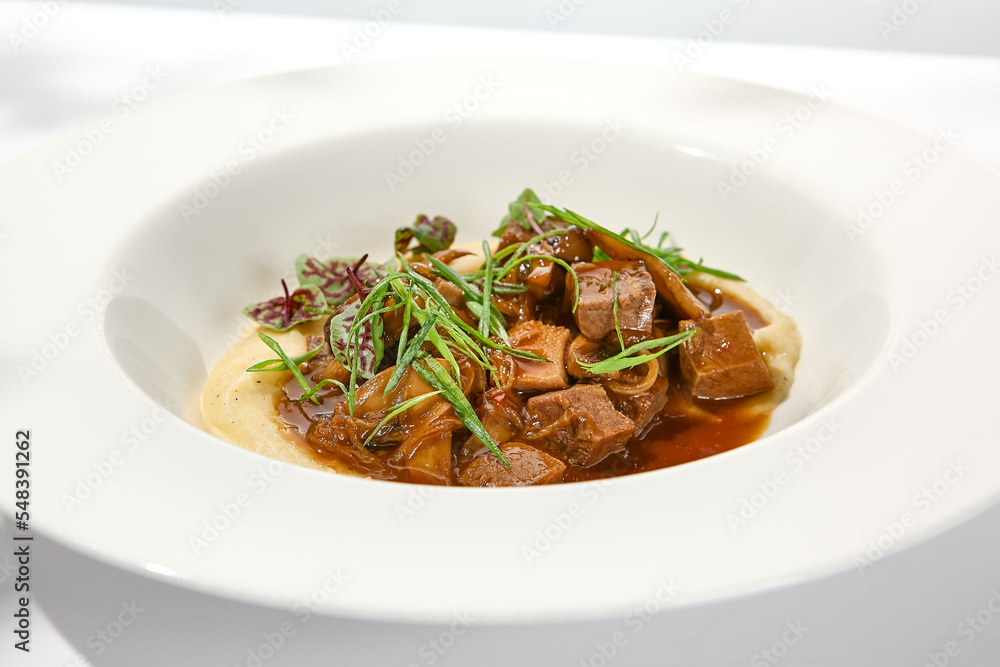 Elegant stew beef with mashed potatoes in restaurant. Beef bourguignon on light background with shadows of leaves Braised black angus meat with potato cream in summer menu Elegant stew beef with mashed potatoes in restaurant. Beef bourguignon on light background with shadows of leaves Braised black angus meat with potato cream in summer menu