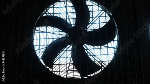 Huge industrial fan spins around behind iron mesh. Process of working cooling ventilation system in factory building for reducing heat during work closeup