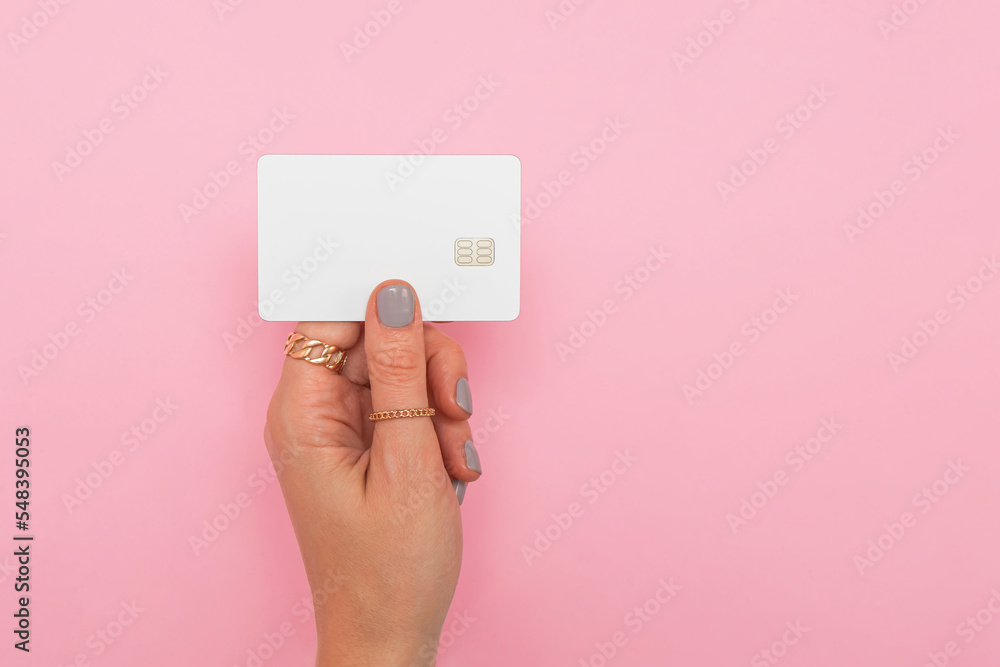 Woman's hand holding white credit or debit card with chip over the pink background Woman's hand holding white credit or debit card with chip over the pink background