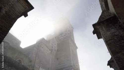 Tilt up shot of an old church with old walls in the town of medina sidonia in cadiz spain with view of columns and the church tower in an abstract historical architecture during sunrise. Slow Motion photo