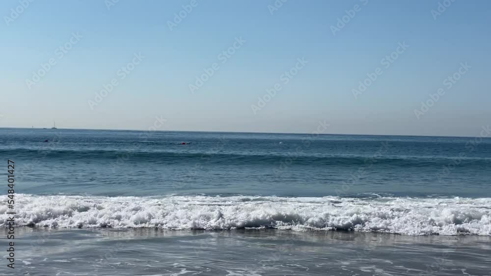 Slow motion handheld closeup of small waves on a beach with some swimmers doing a competition in Cascais Slow motion handheld closeup of small waves on a beach with some swimmers doing a competition in Cascais