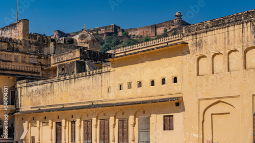 The weathered walls of the ancient Amber Fort are made of orange sandstone. Decorative elements, domes, spires are visible. Blue sky. India. Jaipur