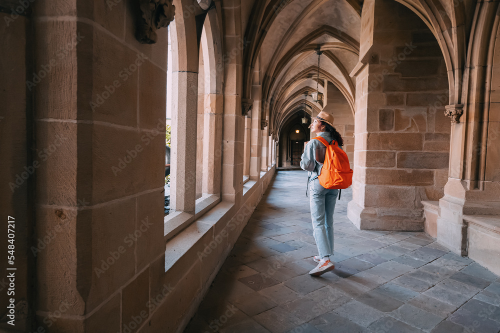 A girl traveler and tourist walks in the hall of an ancient monastery or the courtyard of the cathedral - obrazy, fototapety, plakaty 