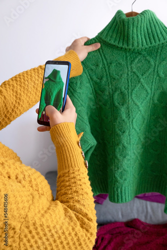 woman with phone in hand, taking photo of clothes to sell second-hand photo