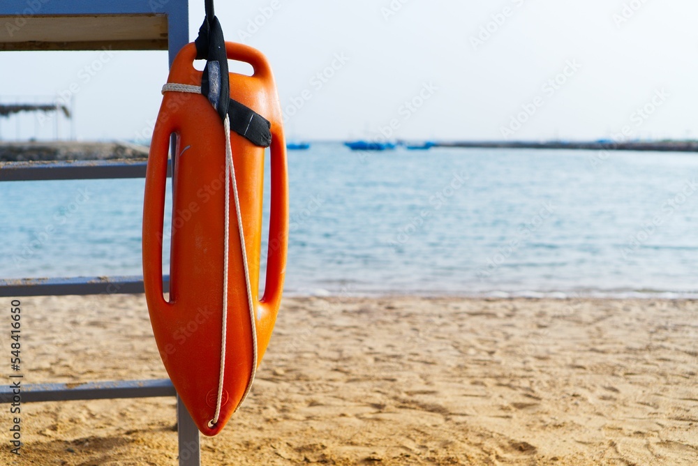 Obraz premium Sandy beach with an orange rescue buoy on an iron stand with the sea in the background, Egypt