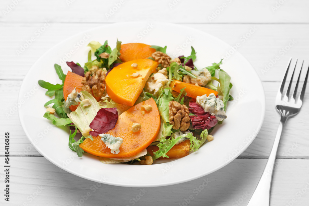 Delicious persimmon salad and fork on white wooden table, closeup