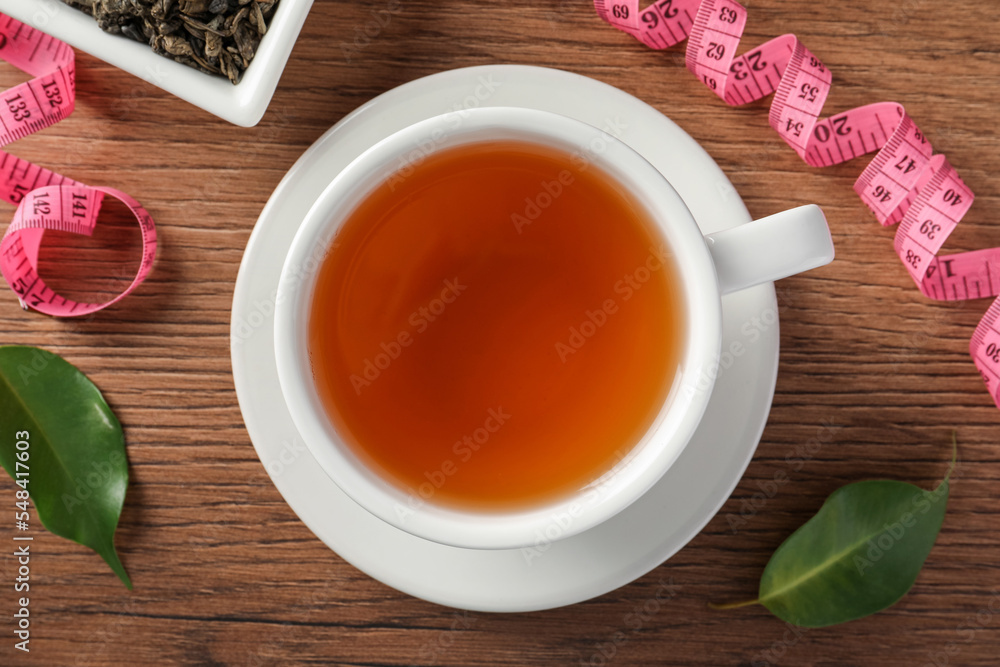 Cup of herbal diet tea and measuring tape on wooden table, flat lay. Weight loss concept Cup of herbal diet tea and measuring tape on wooden table, flat lay. Weight loss concept