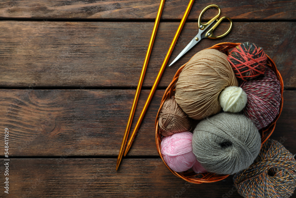 Soft woolen yarns, knitting needles and scissors on wooden table, flat lay. Space for text