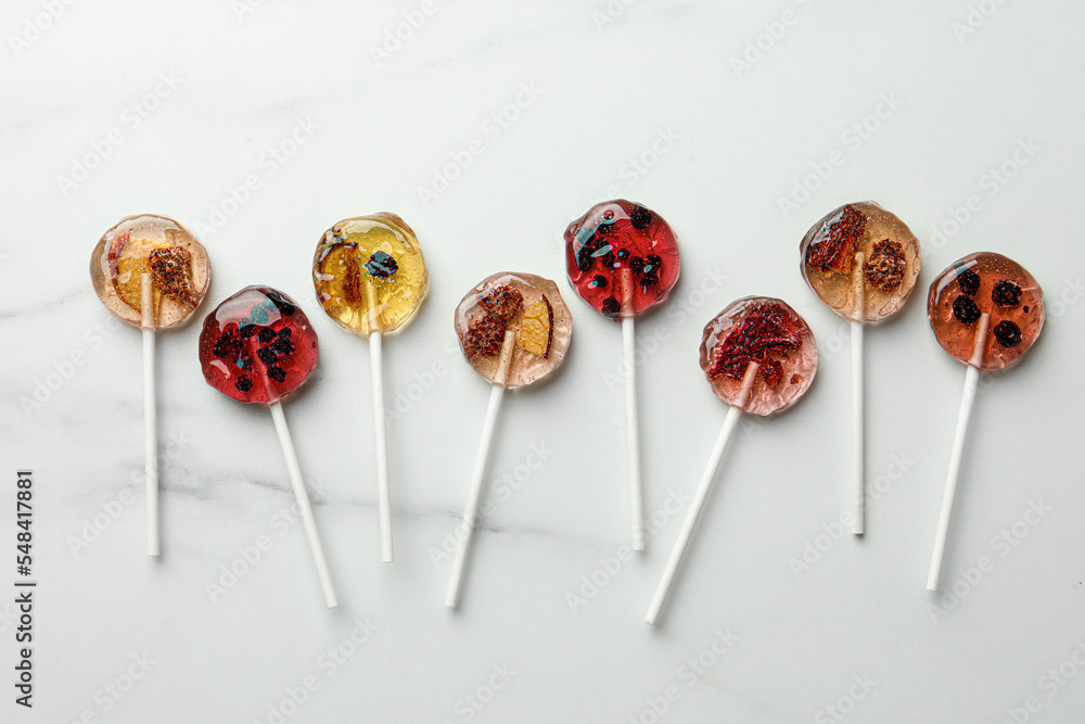 Sweet colorful lollipops with berries on white marble table, flat lay Sweet colorful lollipops with berries on white marble table, flat lay