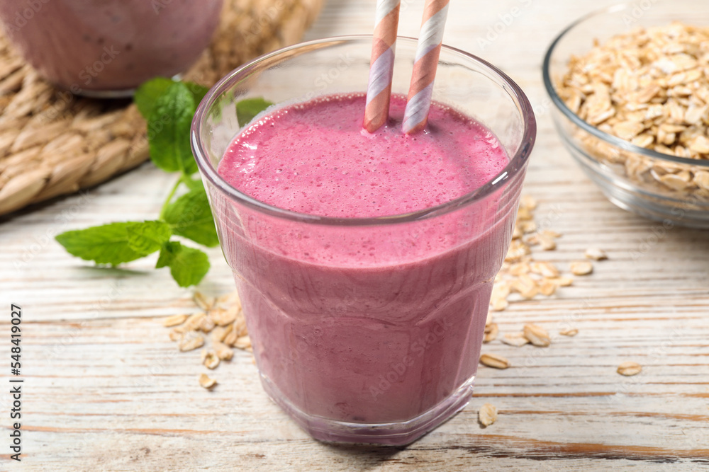 Glass of blackberry smoothie with straws, mint and oatmeal on light wooden table, closeup Glass of blackberry smoothie with straws, mint and oatmeal on light wooden table, closeup