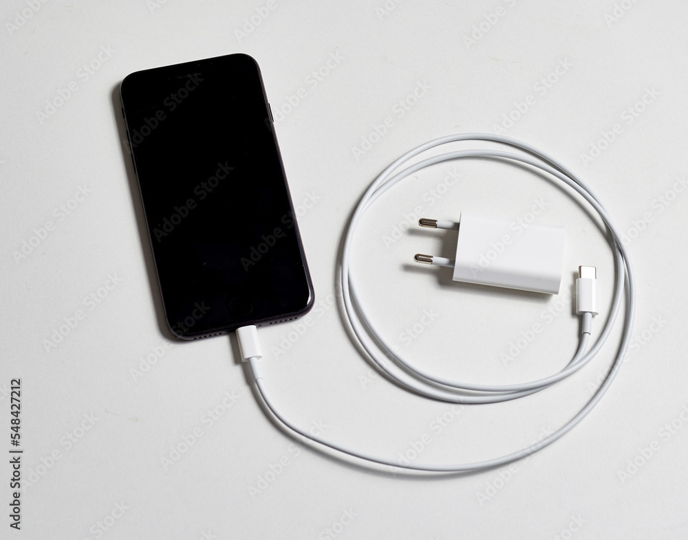 Black smartphone and white charger with cable concept energy and battery charge Black smartphone and white charger with cable concept energy and battery charge