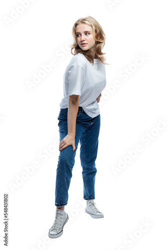 A cute teenager girl in jeans and a white T-shirt is standing. Full height. Isolated on white background. Vertical.