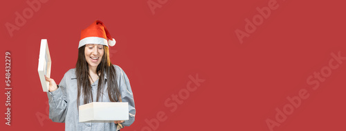 banner di una giovane ragazza che apre la scatola dei regali mentre indossa un bel cappello di natale su sfondo rosso  in studio con spazio libero 