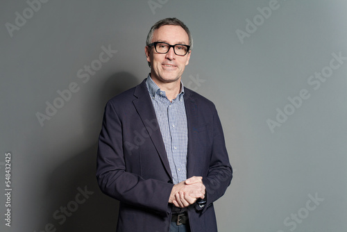 Portrait of happy mature businessman in blue suit and eye glasses against grey studio wall background
