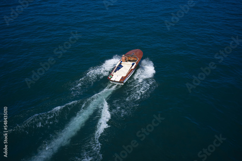 Expensive classic wooden boat with a man at the helm, top view from behind the movement on the water.