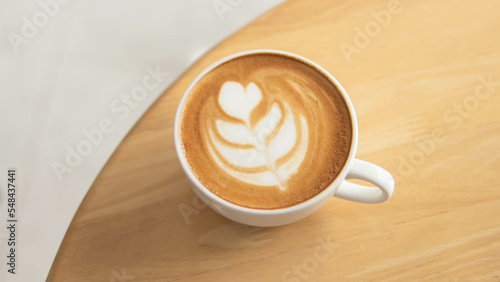 White cup of art latte on wood background standing on a table in a cafe. Foam flower on top of the cup.Little spoon and plate.Close up coffee cup on wooden table.